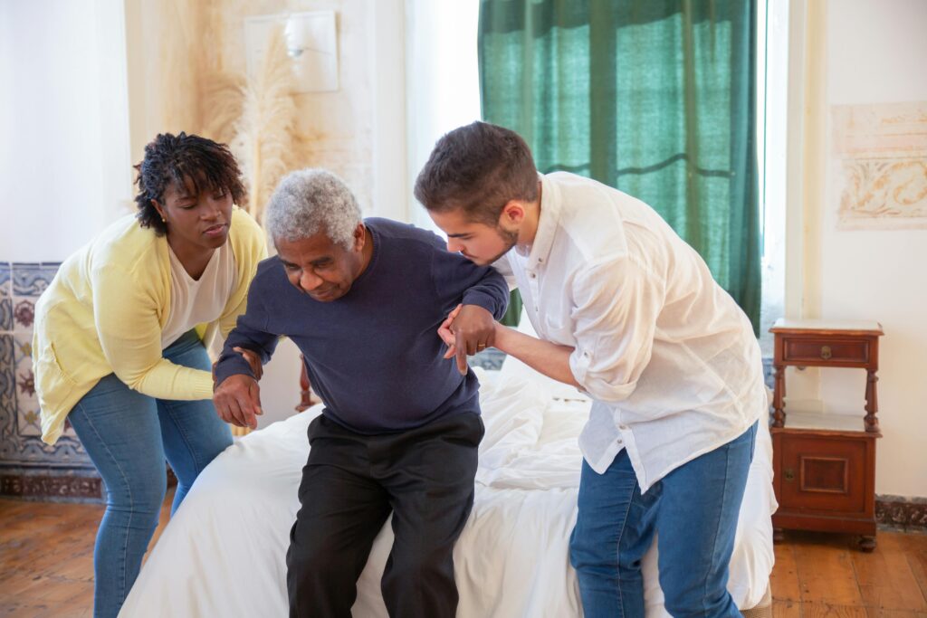 pexels-photo-7551686-7551686 An elderly man receiving assistance from caregivers in a cozy home environment.