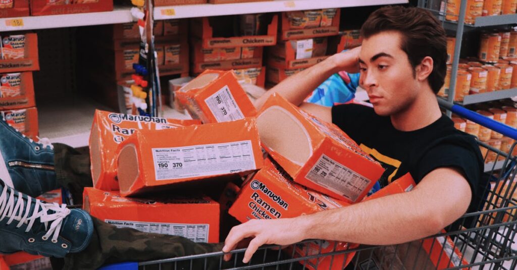 pexels-photo-3427609-3427609 A man lounging in a shopping cart filled with Maruchan ramen in a supermarket aisle.