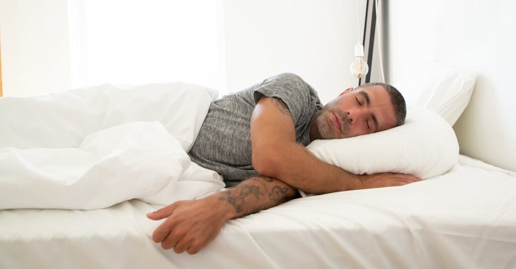 pexels-photo-5990948-5990948 Adult man sleeping soundly on a white bed, tattoo visible, in a bright room.